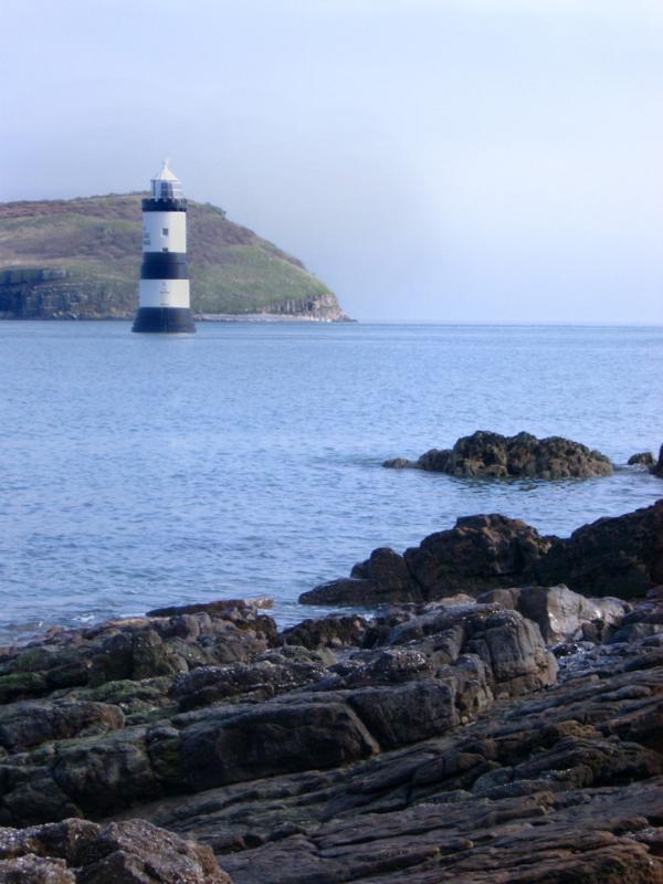 View across the ocean of the distinctive black and white tower of the Trwyn Du Lighthouse, Anglesey, Wales
