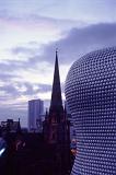 Modern curved exterior facade of the Bullring Shopping Centre with St Martins spire in the background at dusk, Birmingham, UK