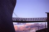 Enclosed glass skywalk bridge on the Bullring Centre, Birmingham with the silhouettes of peole crossing between the buildings against a colorful sunset sky