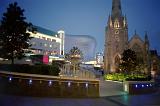 View of an urban square with church and spire in central Birmingham with the Bullring shopping centre in the background at night
