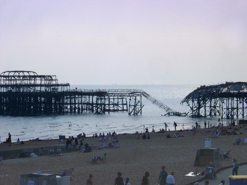 Remnants of the badly damaged fire damaged Brighton pier partially collapsed into the sea with people on the beach in the foreground