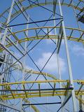 Details of the metal framework of a roller coaster ride at an amusement park against a sunny blue sky