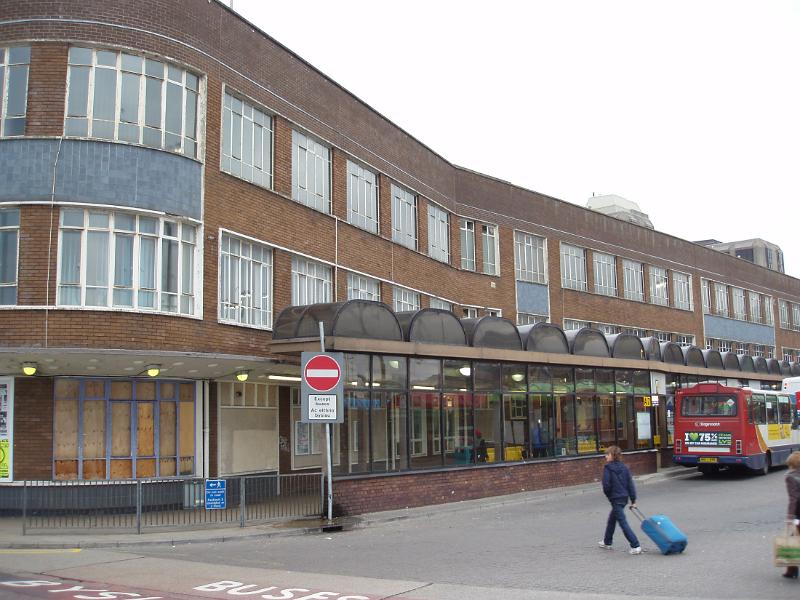 View of the Central Bus Station, Cardiff, Wales with a row of shelters along the exterior of the depot and a woman walking past with her suitcase as a bus loads passengers in the background