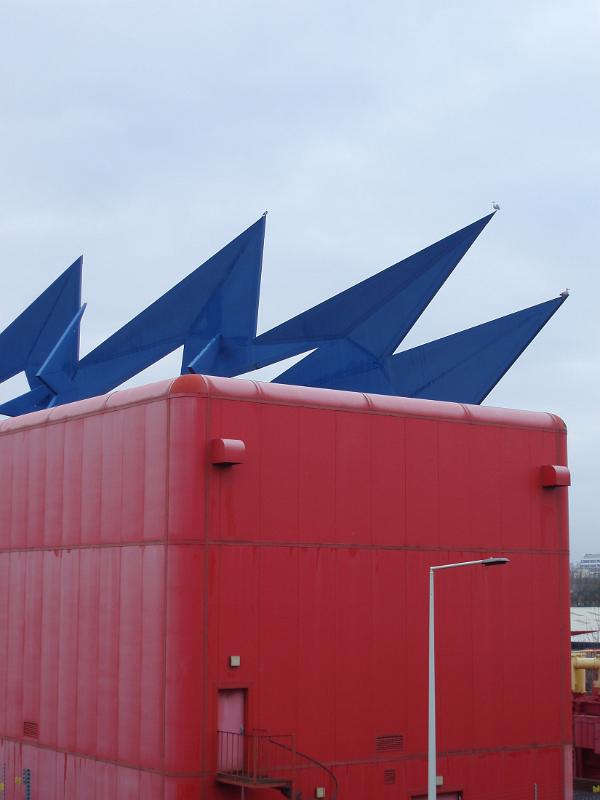 Contemporary art on a powerbox substation in the docklands in Cardiff Bay, Wales with a colorful blue zigzag electric spark icon mounted over a red electricity substation
