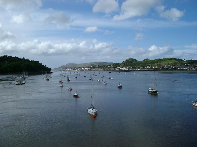 Boats and small yachts or sailboats anchored in a scenic tidal estuary with the coastline behind under a blue summer sky with clouds