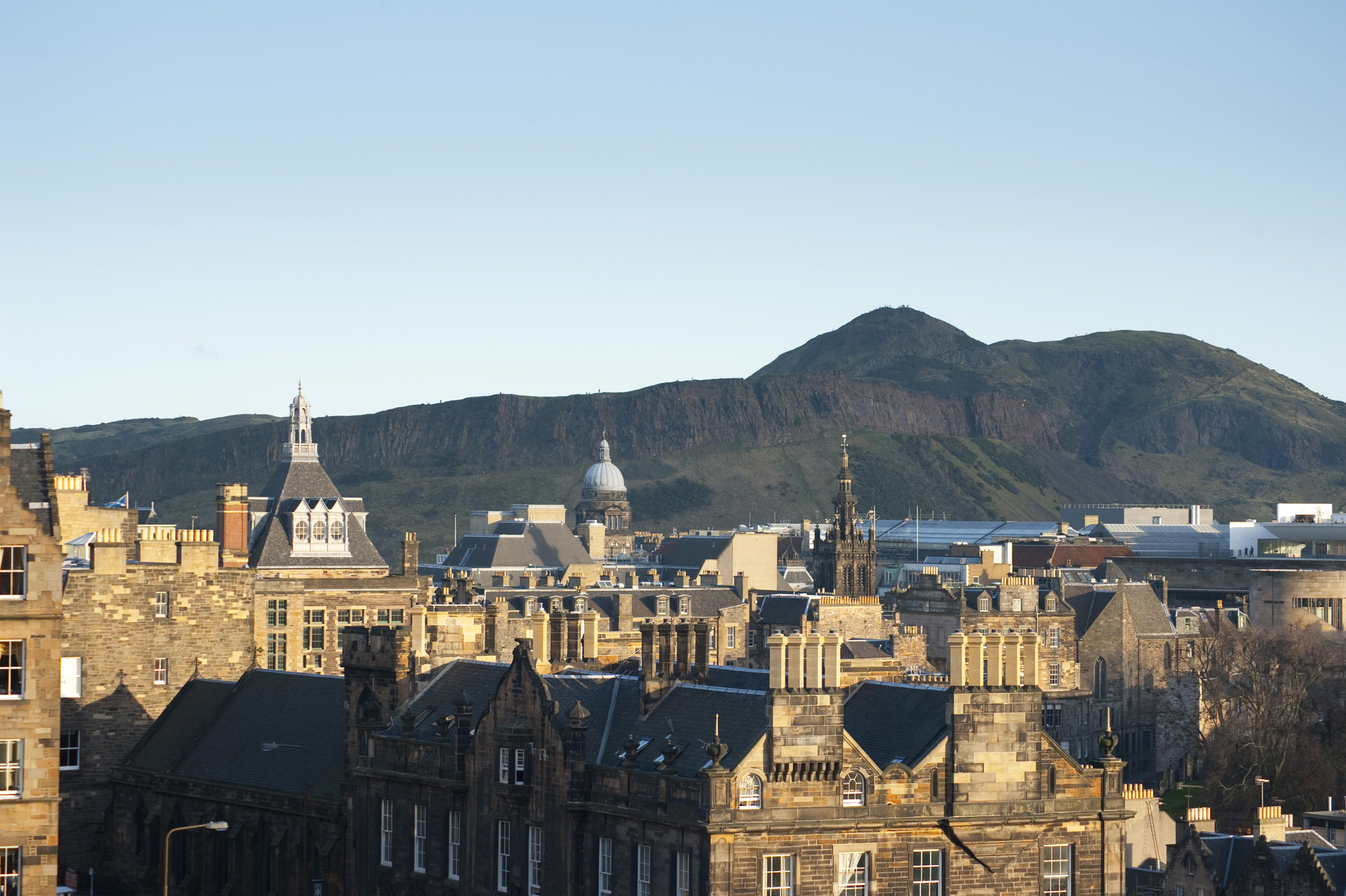 an image of buildings in edinburgh, with salsbury crags and arthurs seat hill behind