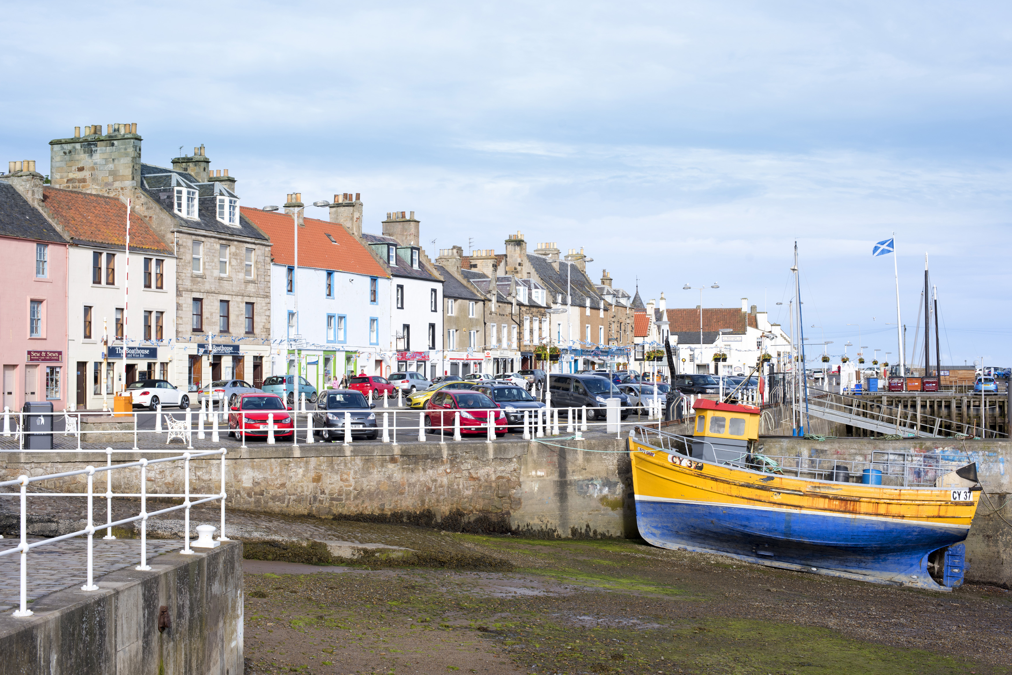 an image of Colorful fishing boat in Anstruther harbour, Scotland beached on the sand at low tide with a view of waterfront buildings behind
