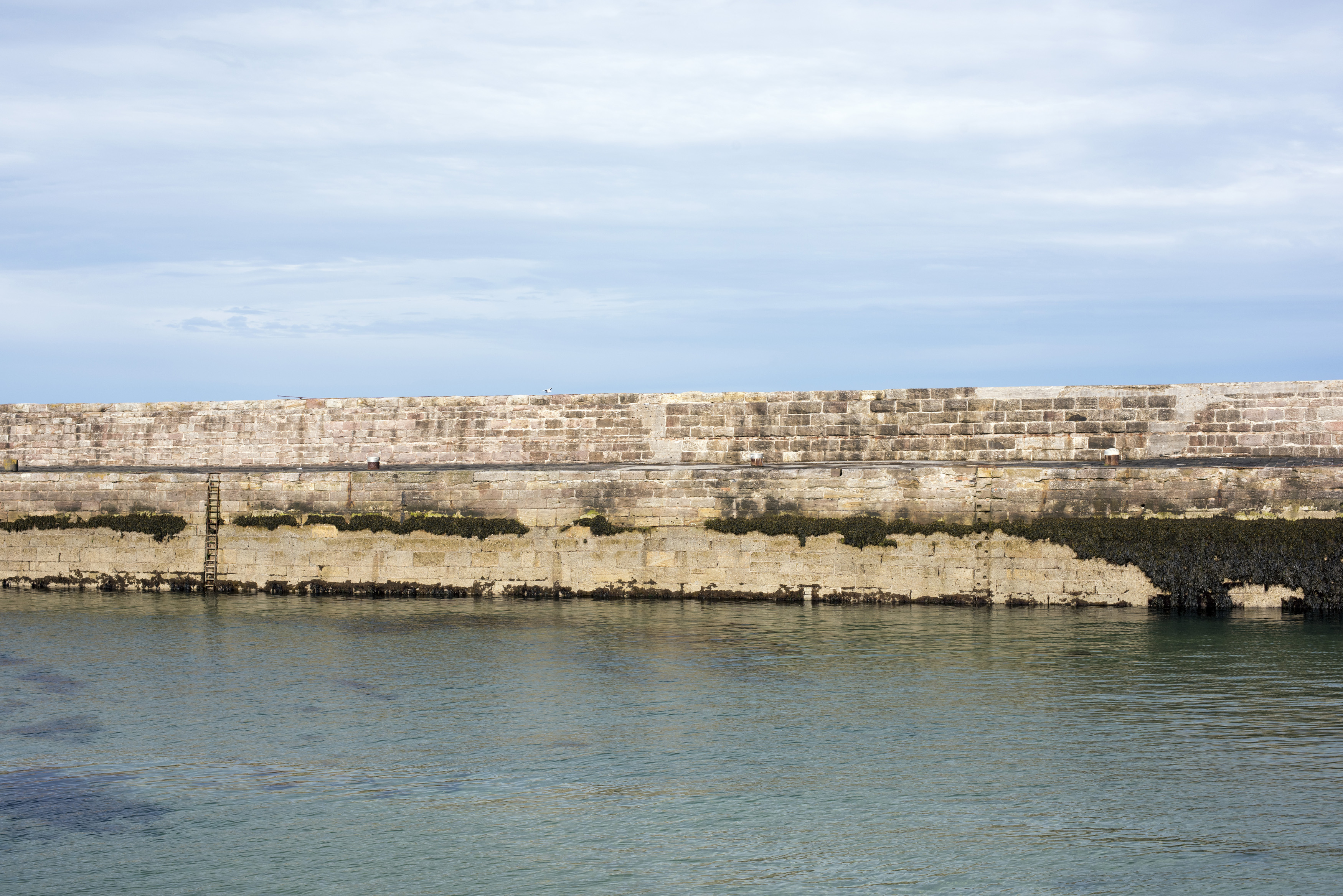 an image of Seawall on the harbour or marina, Anstruther, Scotland with sheltered water in the foreground for safe mooring