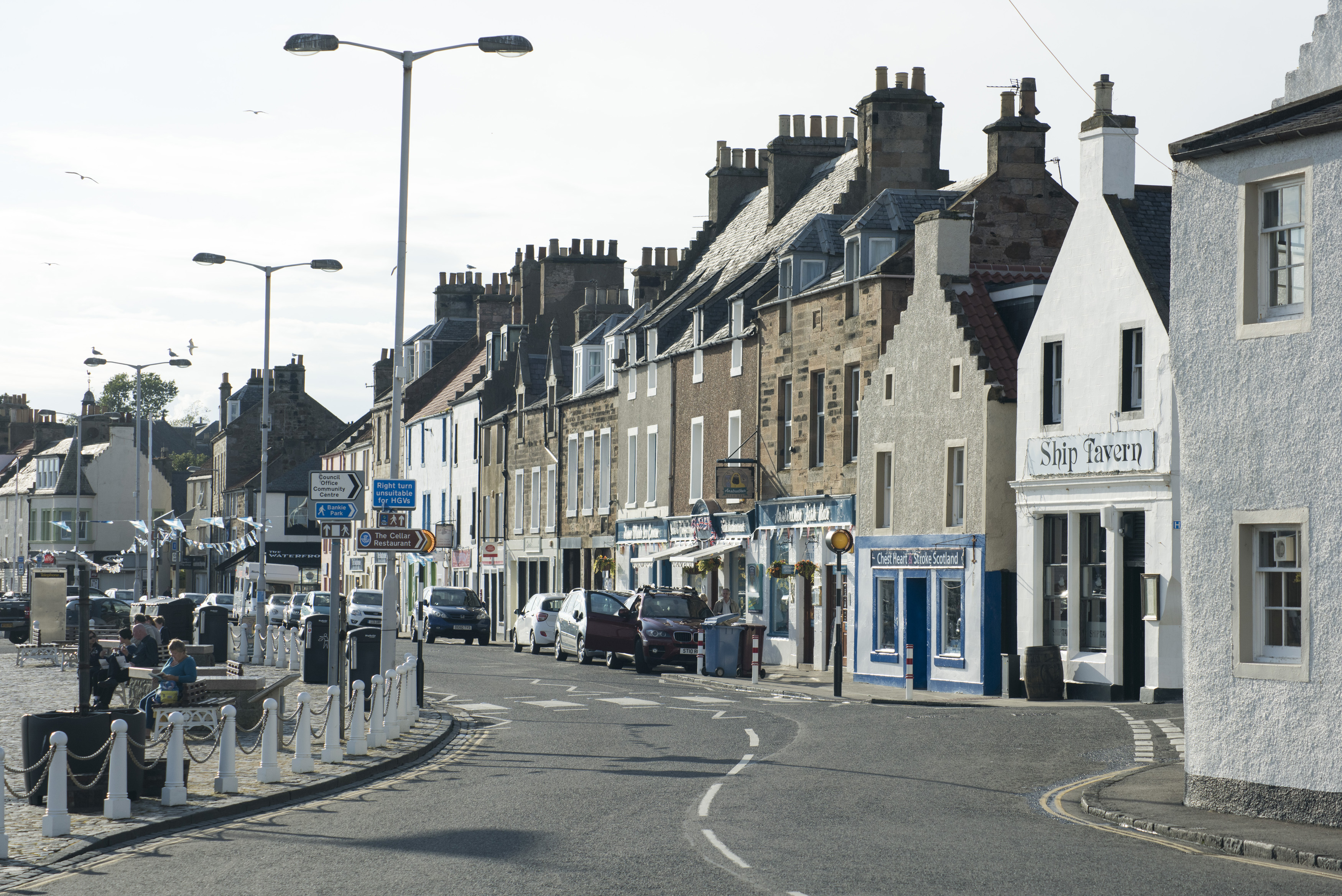 an image of Empty winding two lane road with parked cars early in the morning in Anstruther, Scotland
