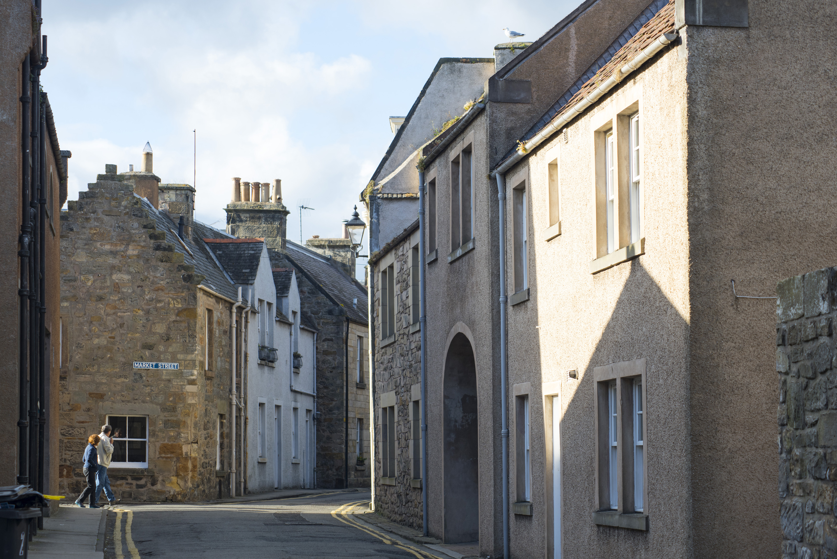 an image of Two people walking through a narrow back street past historic cottages and townhouses, St Andrews, Scotland