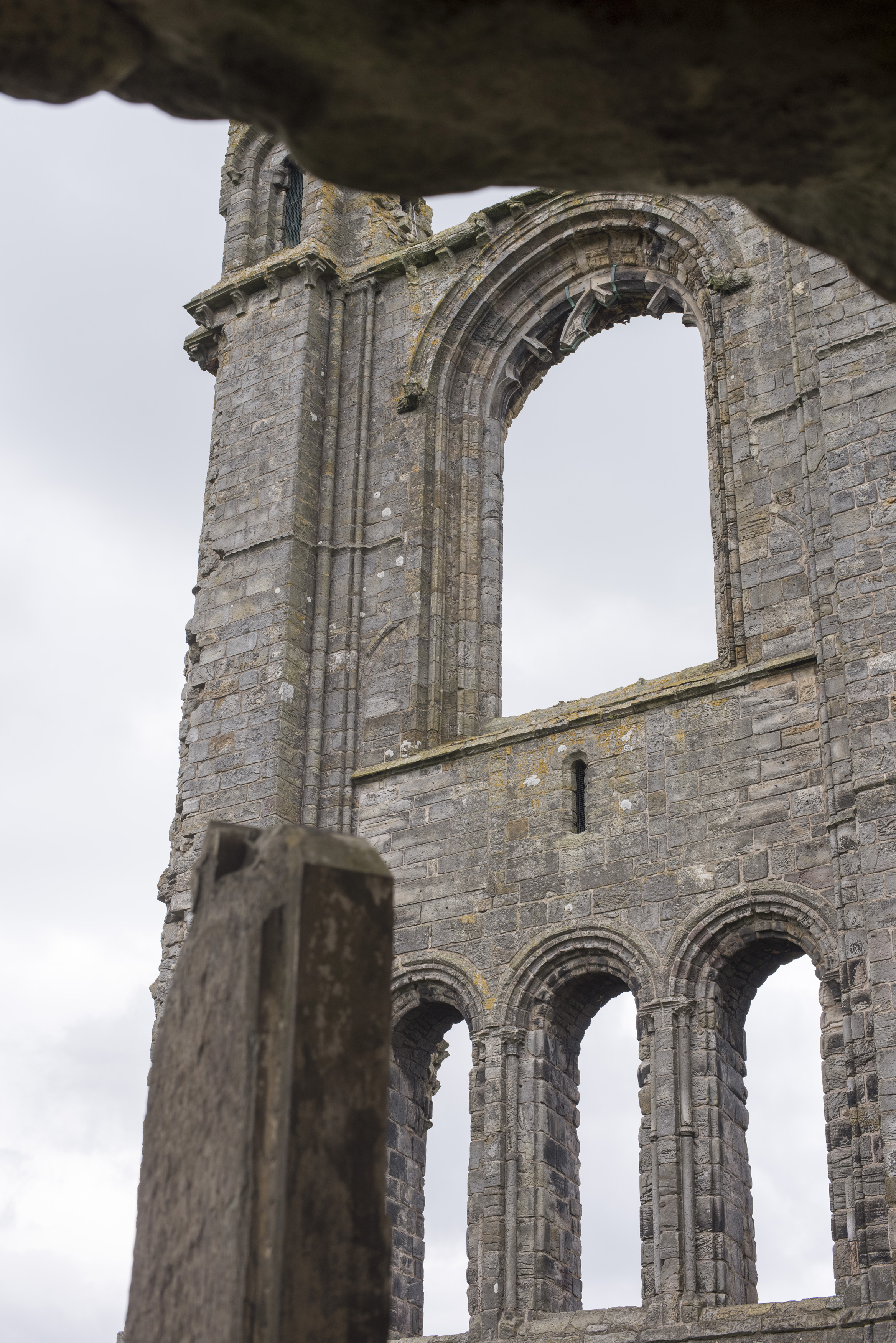 an image of Detail of the St Andrews Cathedral ruins, Scotland showing the arched gothic windows in an ancient stone wall with view through to a hazy sky