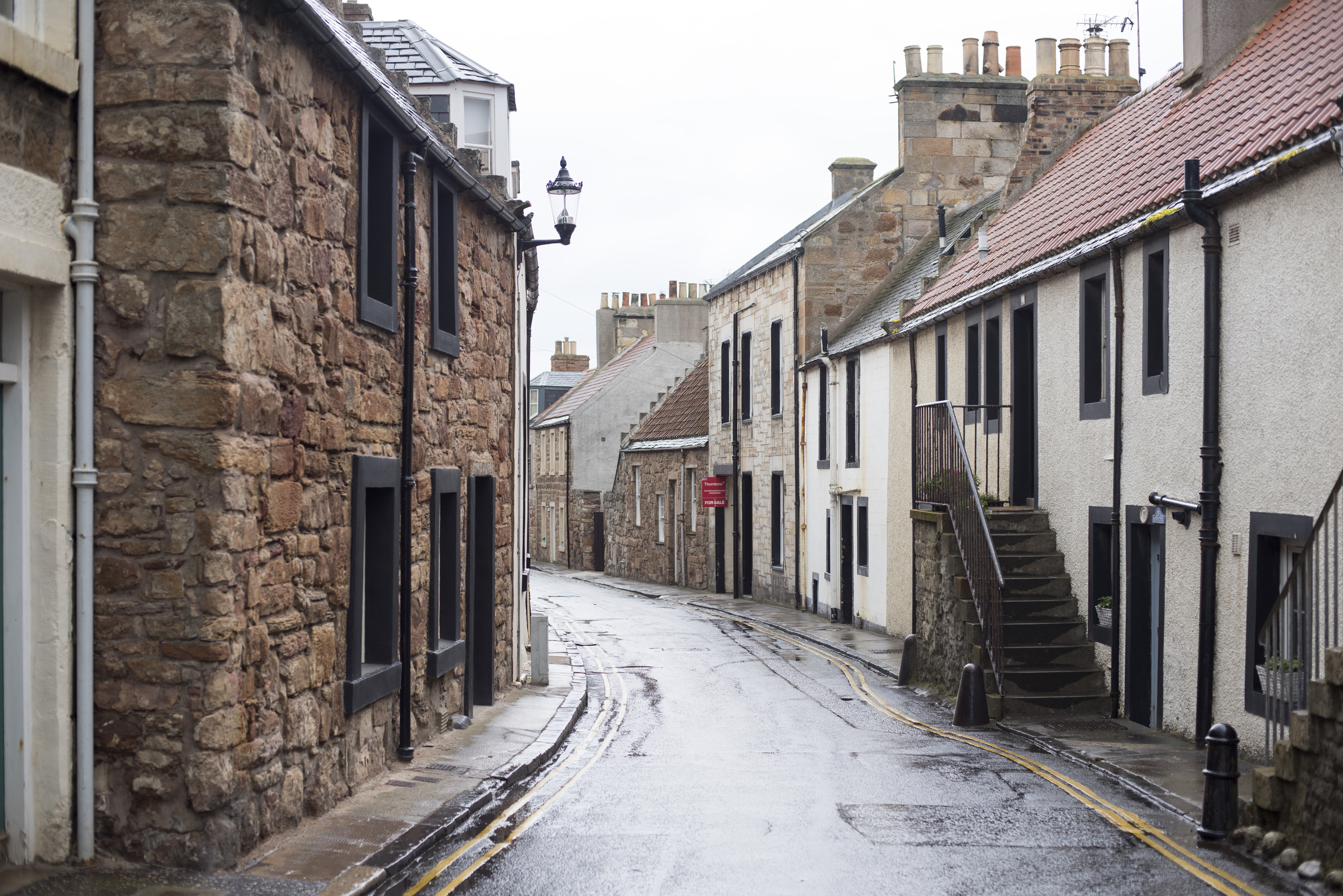 an image of Narrow street in Cellardyke, Scotland lined with quaint cottages on a rainy overcast day