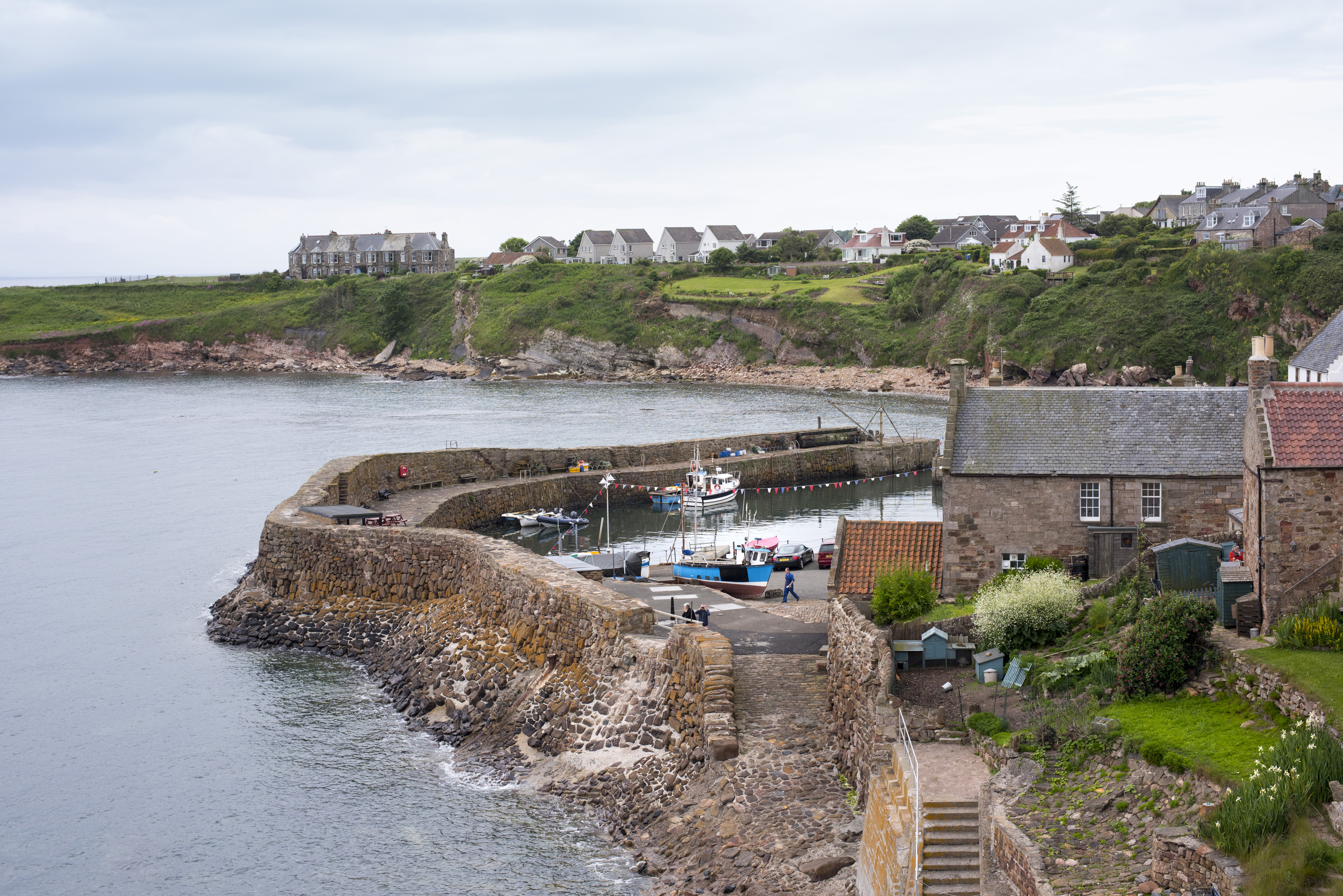 an image of Scenic small boat harbour, Crail, Scotland on the Fife coast with steps leading to a seawall enclosing a sheltered fishing harbor with moored boats