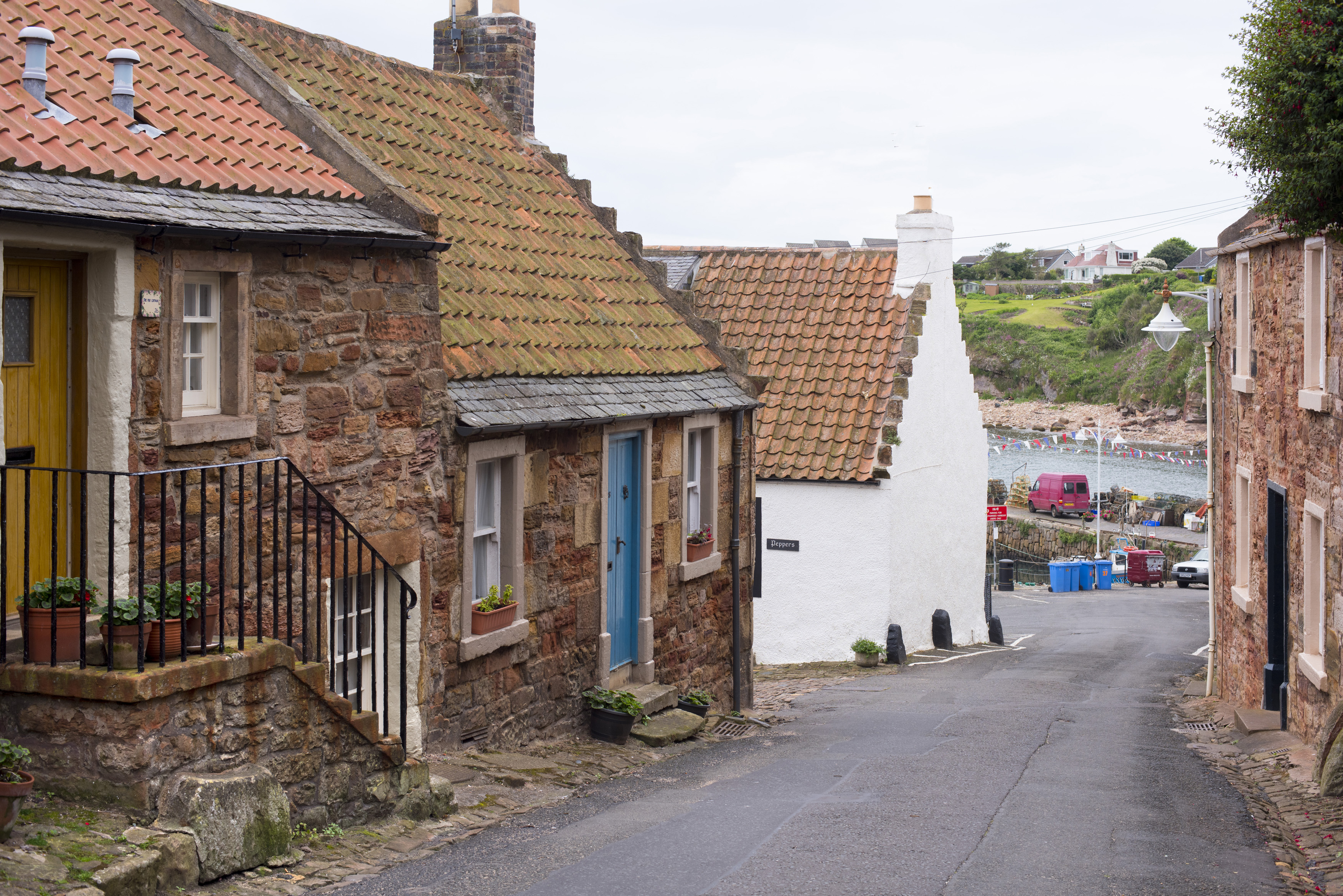 an image of Old stone cottages, Crail, Fife coast, Scotland on a deserted narrow lane leading down to the water and parked cars