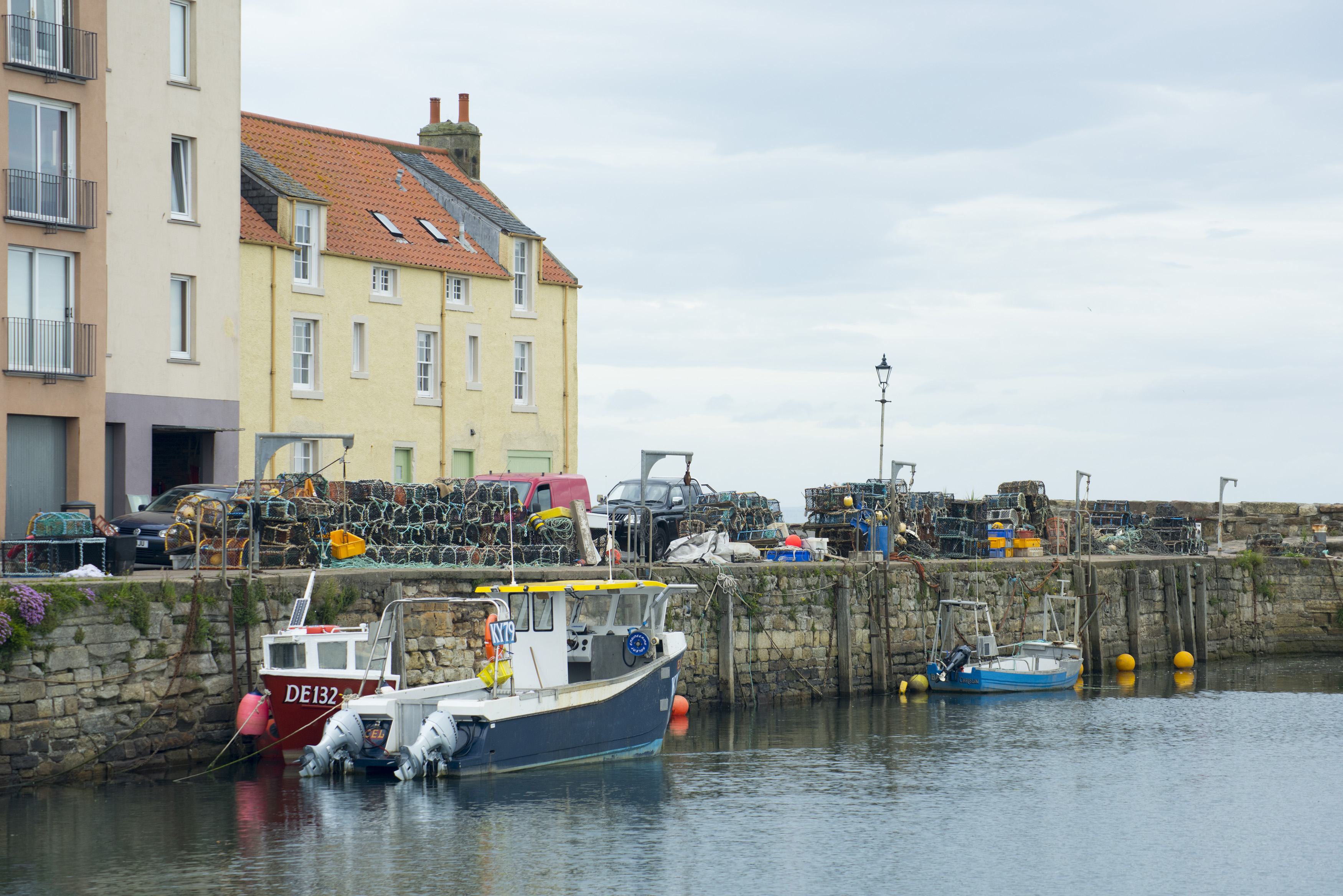 an image of Fishing boats moored in the harbour, St Andrews, Scotland with stacked wire traps on the quay overlooked by waterfront apartments