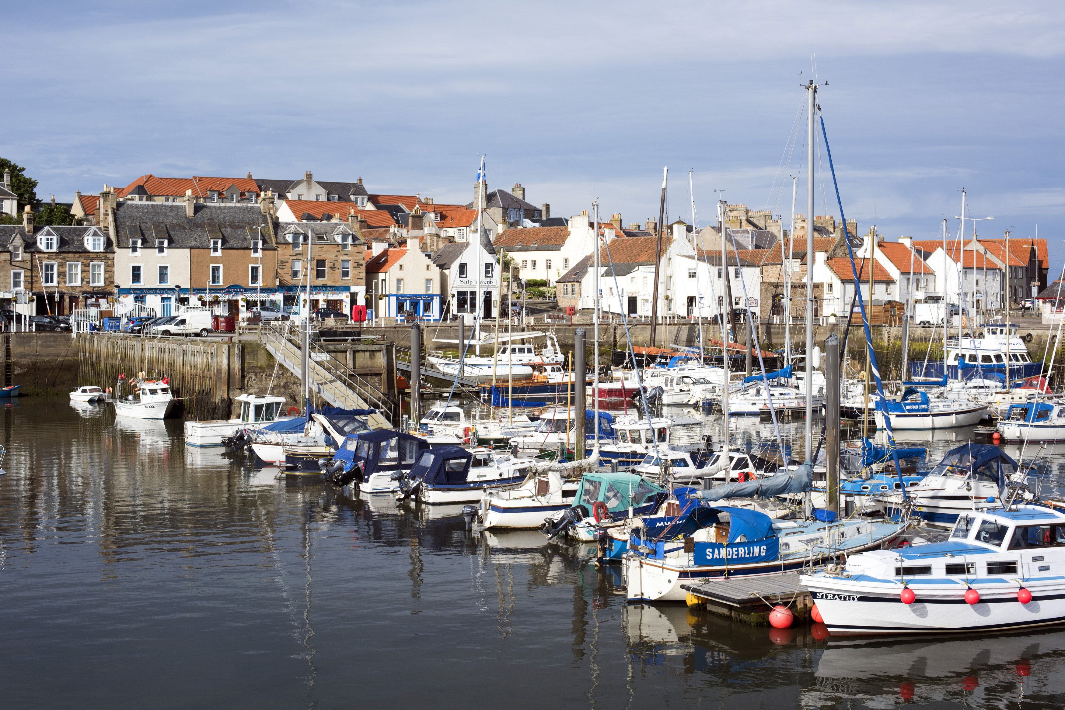 an image of Scenic view of boats moored in Anstruther harbour, Scotland with an assortment of fishing boats, motorboats, sailboats and yachts overlooked by waterfront houses