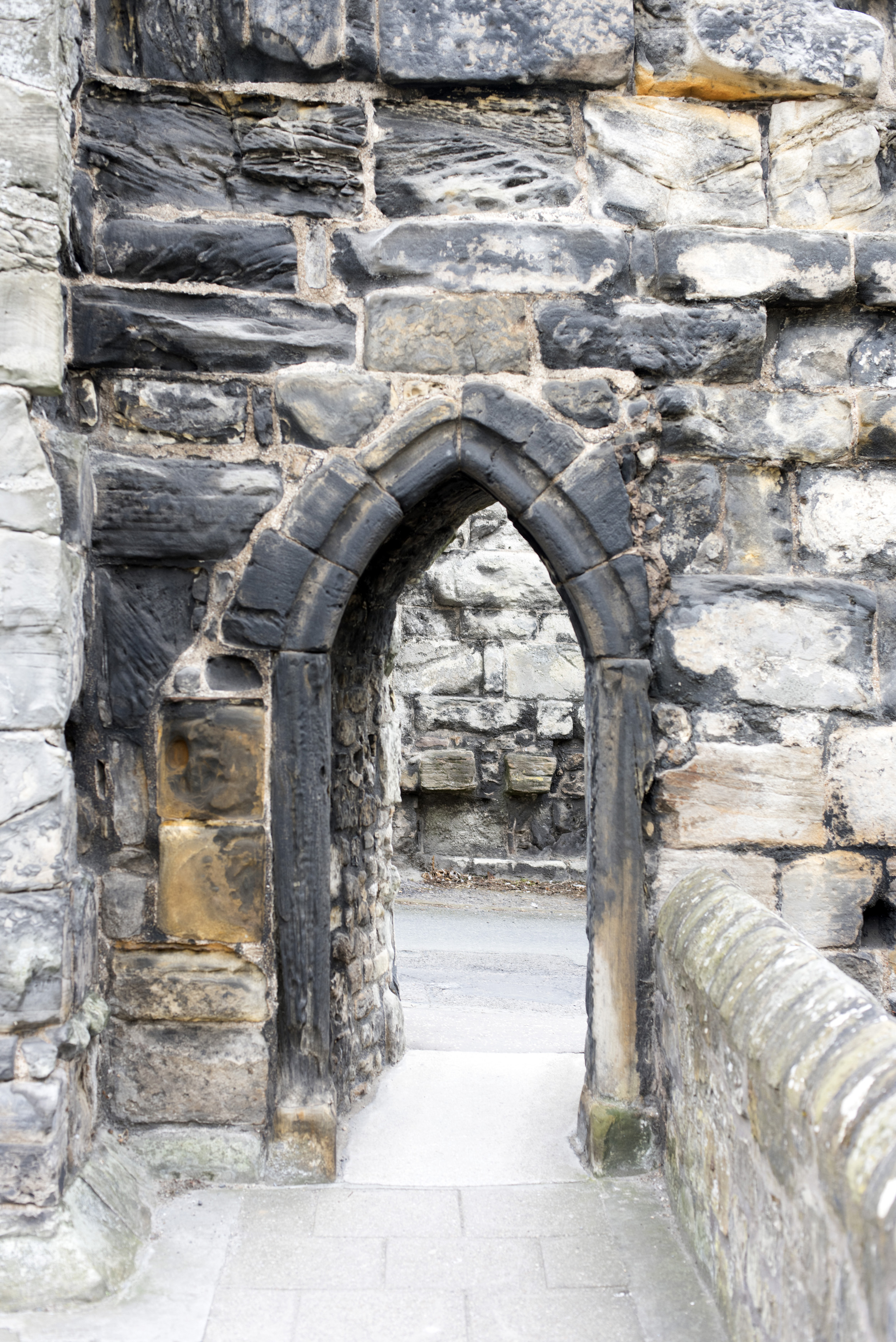 an image of Medieval stone arch in an ancient building with a paved walkway leading through to a road behind
