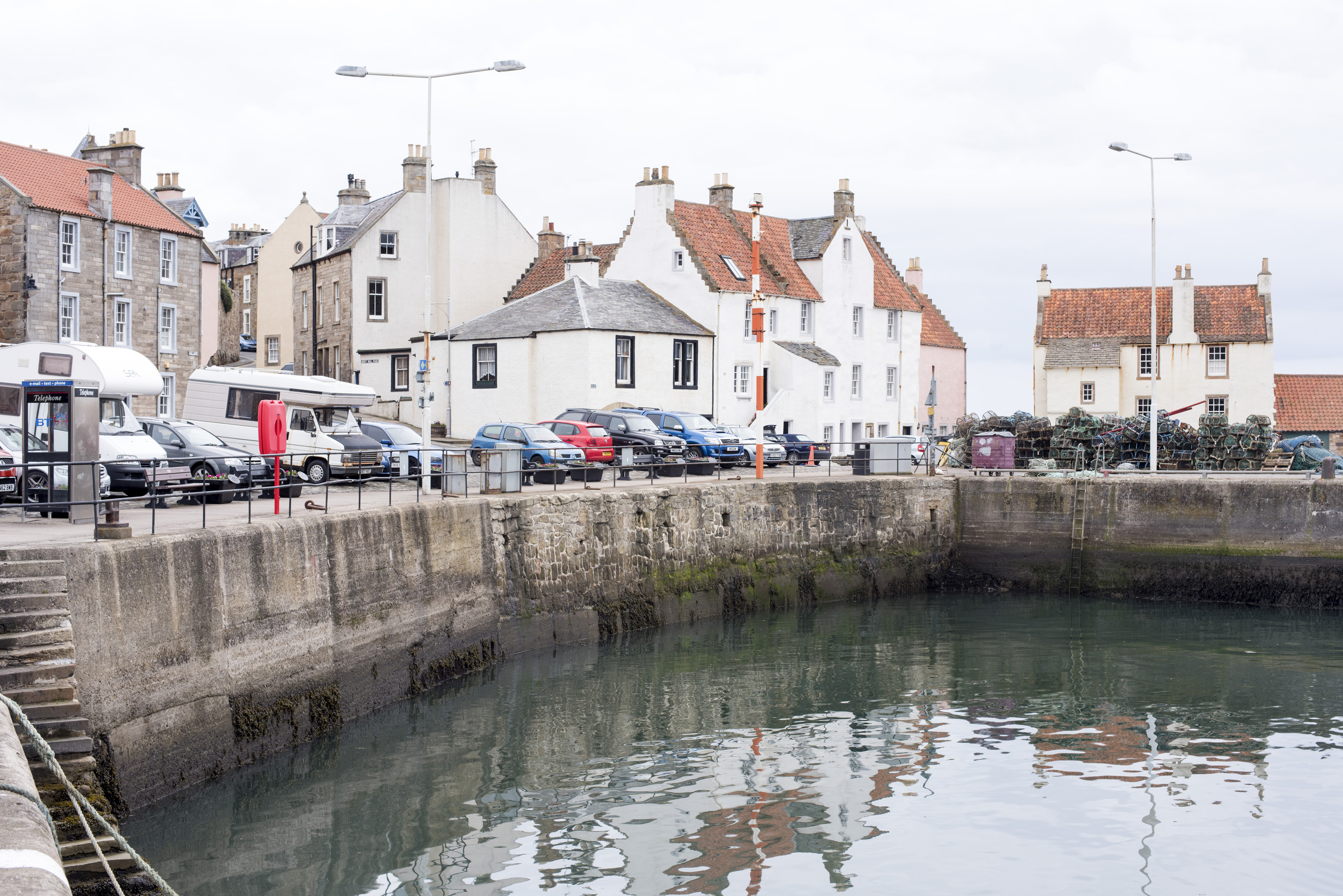 an image of Cars and vans belonging to tourists parked around empty harbor at Pittenweem, Scotland
