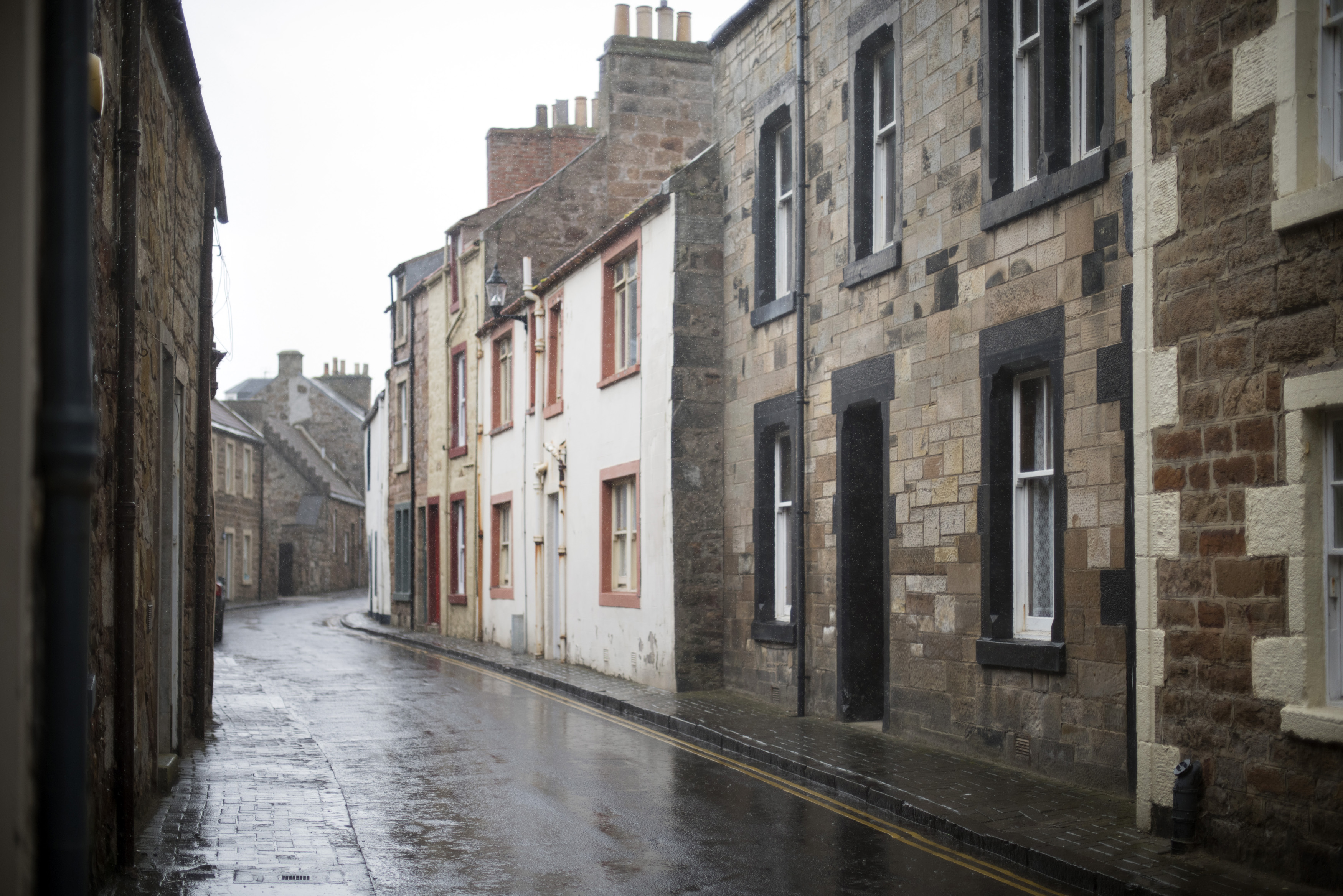 an image of Empty brick road on rainy day in old village lined with stone apartment houses in Scotland
