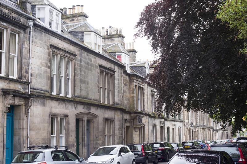 View down street with dark leafed tree hanging over cars in Saint Andrews, Scotland