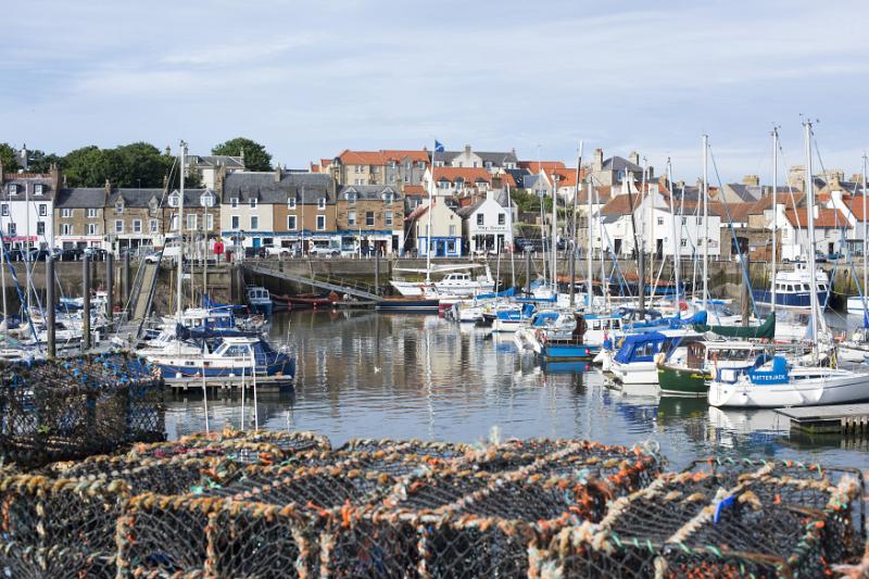 wire fishing traps with fishing and pleasure boats and yachts moored in the harbour overlooked by waterfront houses, Anstruther, Scotland