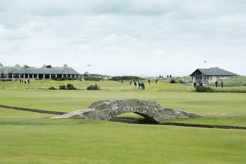 Scenic view of beautiful scottish golf course with a short stone bridge and adjoining buildings in the distance