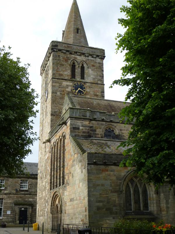 Street level view of tall rectangular clock and bell tower on Holy Trinity Church framed by trees in Saint Andrews, Scotland