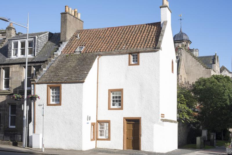 Whitewashed cottage facing onto a street surrounded by old stone buildings , St Andrews, Scotland in a travel and tourism concept
