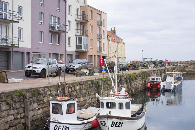 Cozy seaside harbour with small motor boats docked beside stone wall under a cloudy sky
