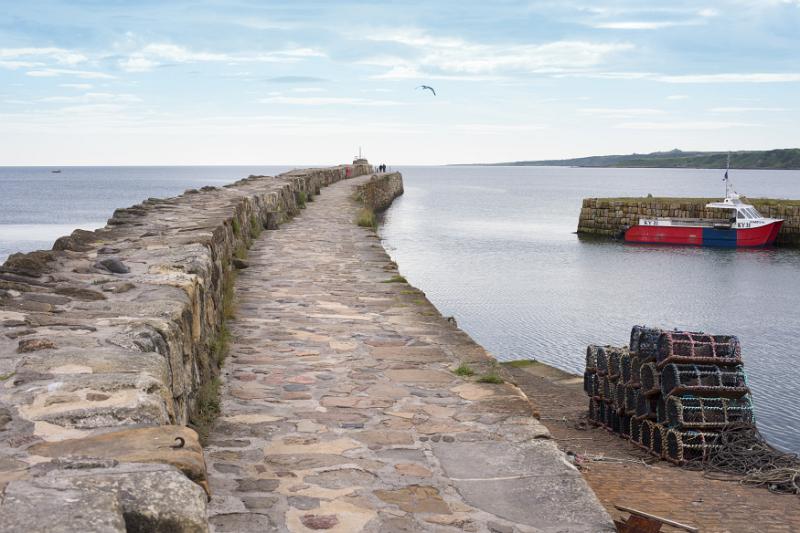 Old stone pier or seawall at the fishing harbour in St Andrews Scotland, UK, with a small fishing boat moored against the quay