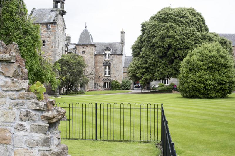 Gated university grounds with lush green lawn and adjoining stone buildings