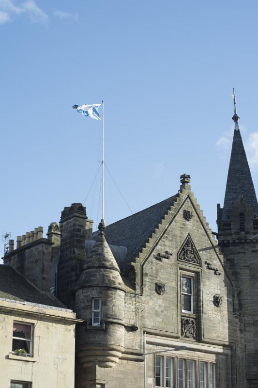 town hall building with with castle like angle tower and flag on top under blue sky in Saint Andrews, Scotland