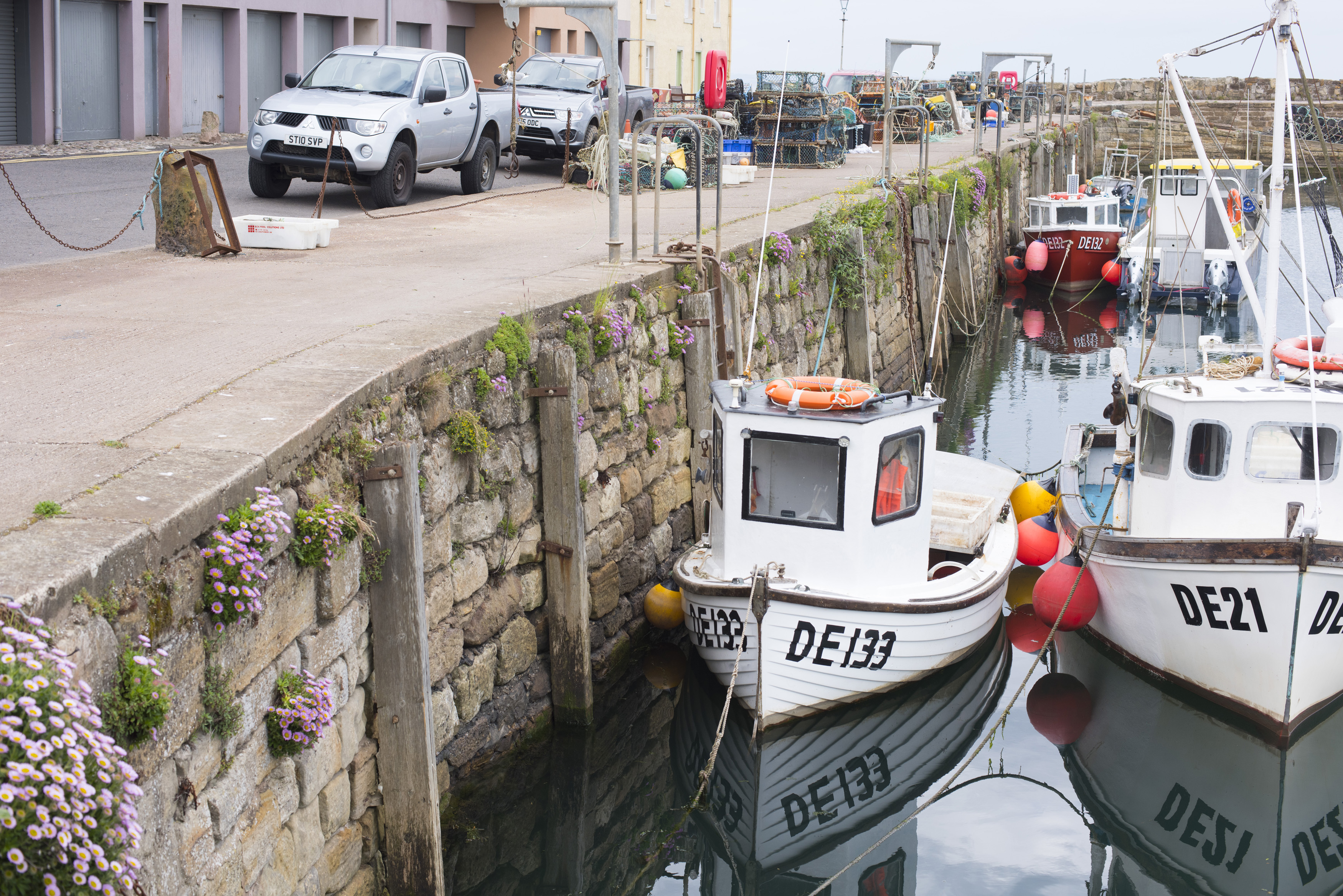 an image of Pair of little white tug boats in low tide water at famous landmark Saint Andrews pier in Scotland