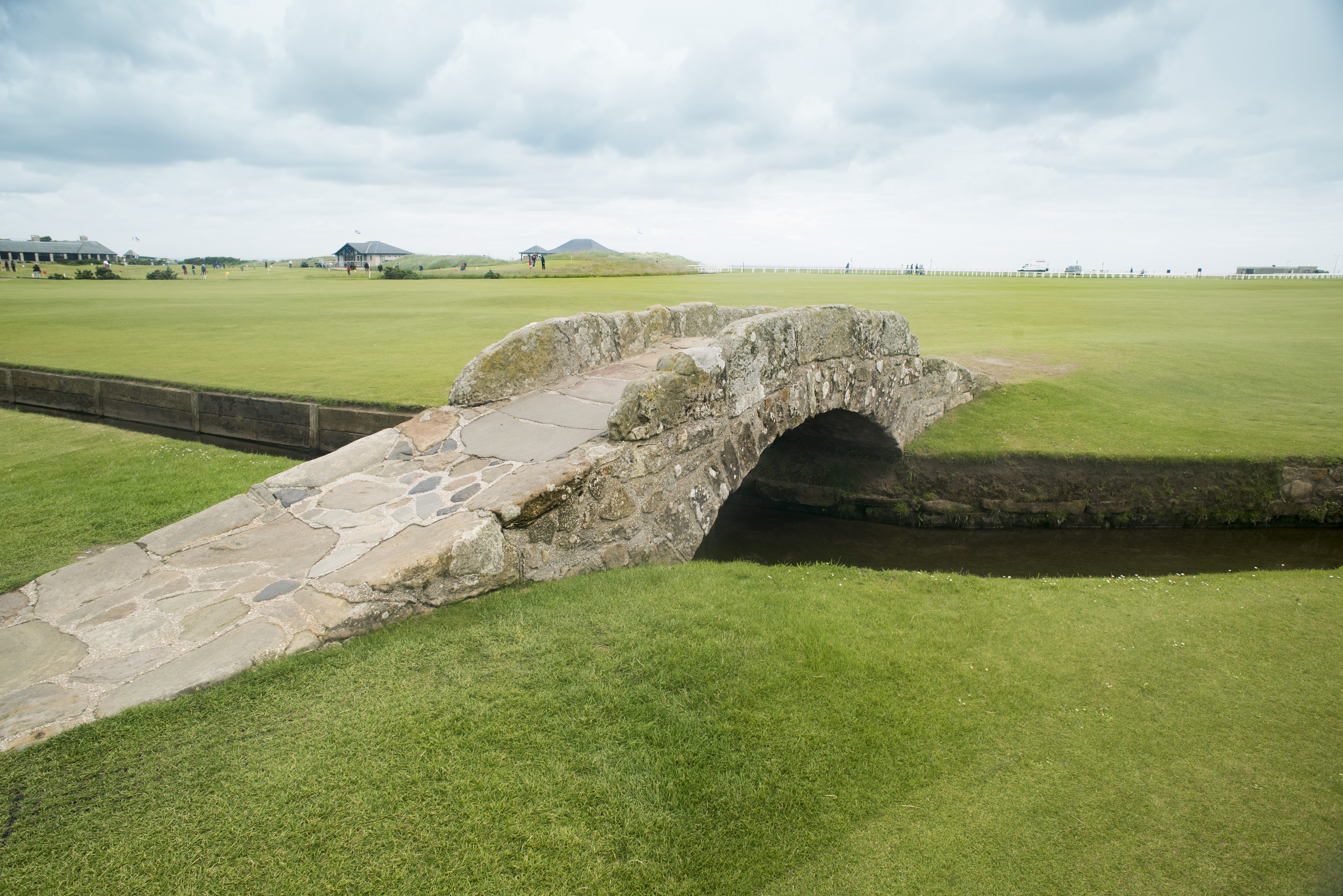 an image of Picturesque old stone Swilken Bridge connecting the fairways on St Andrews gold course in St Andrews, Scotland under a grey cloudy sky