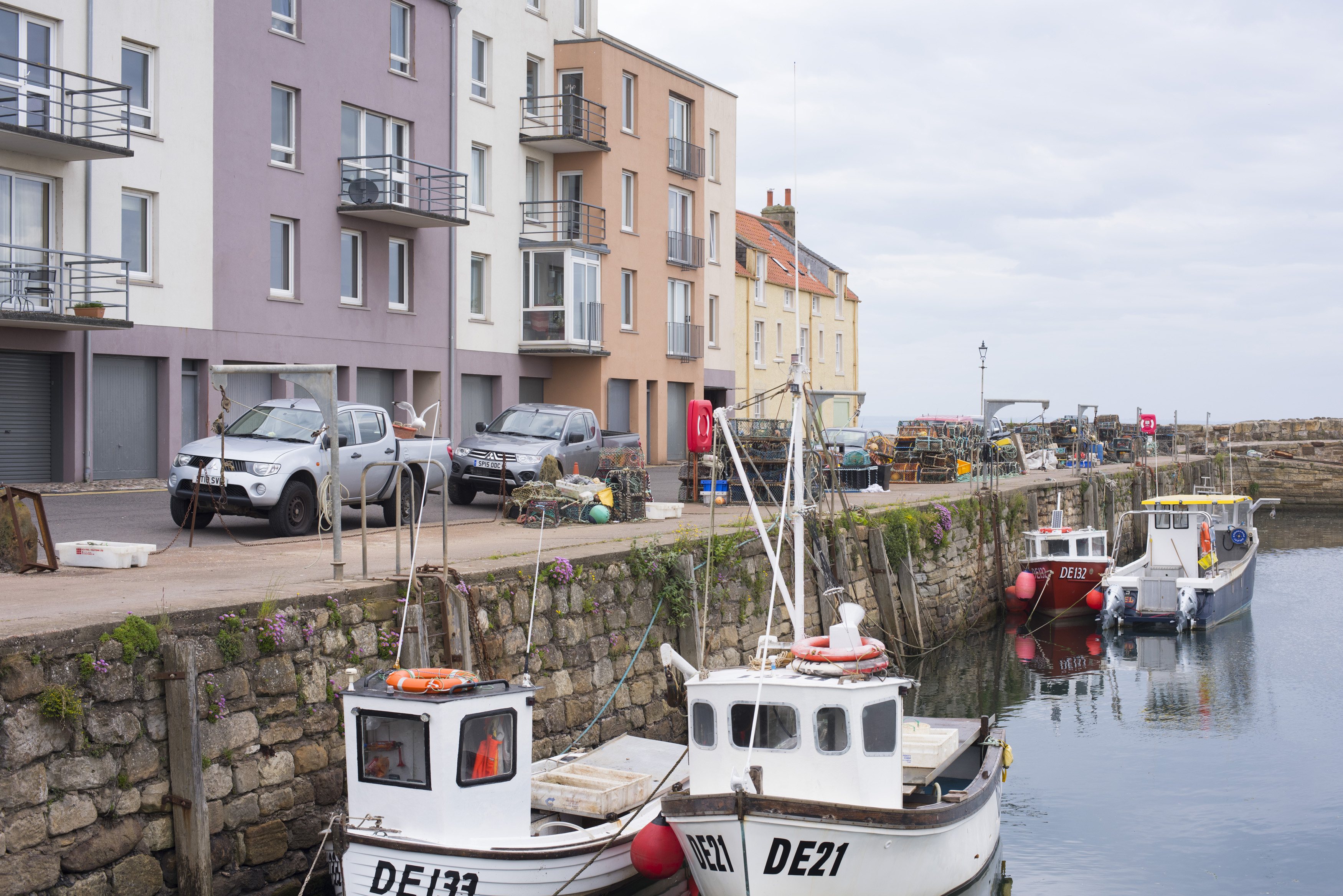 an image of Cozy seaside harbour with small motor boats docked beside stone wall under a cloudy sky
