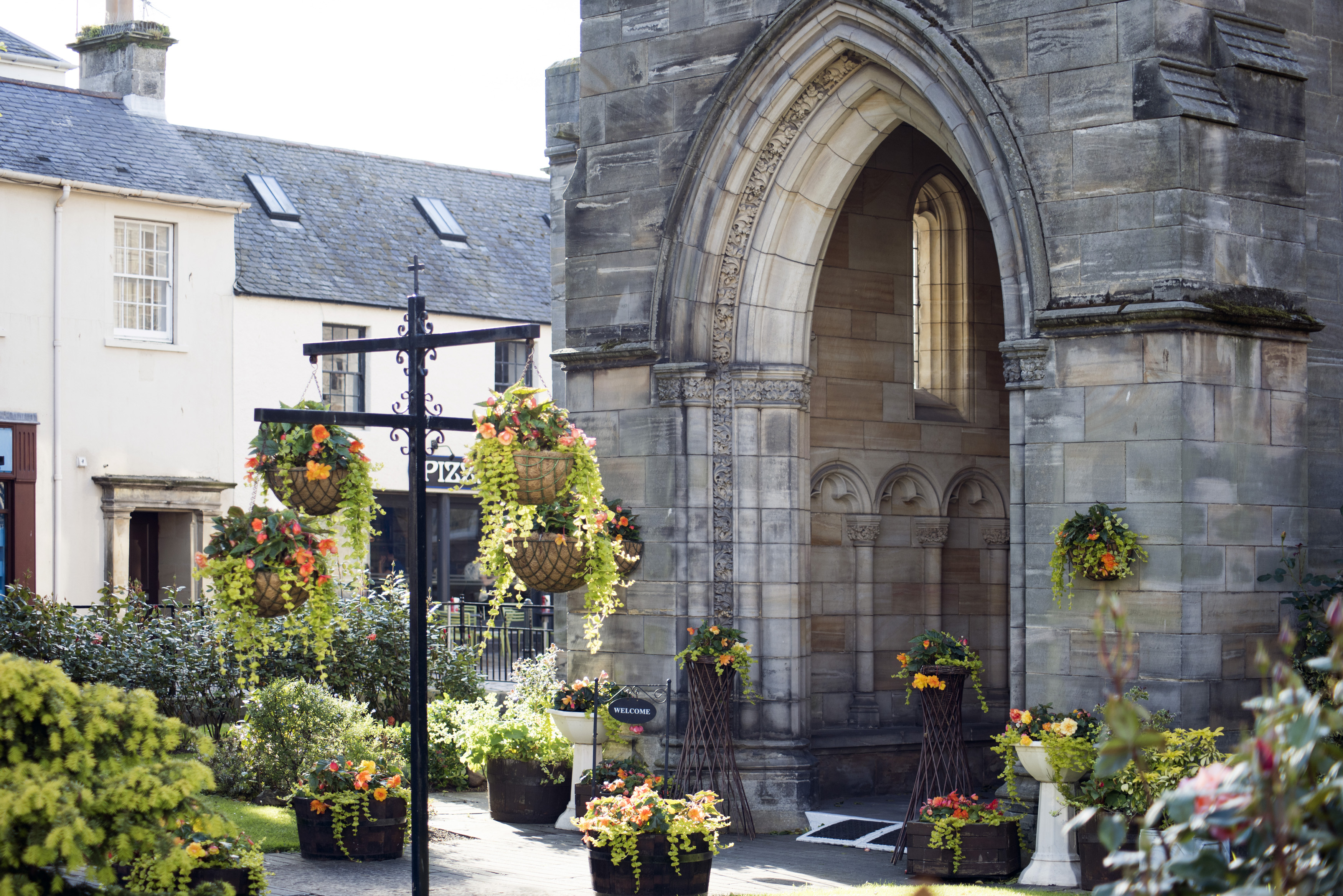 an image of Flowing baskets near old stone church block entrance with arch in Saint Andrews, Scotland