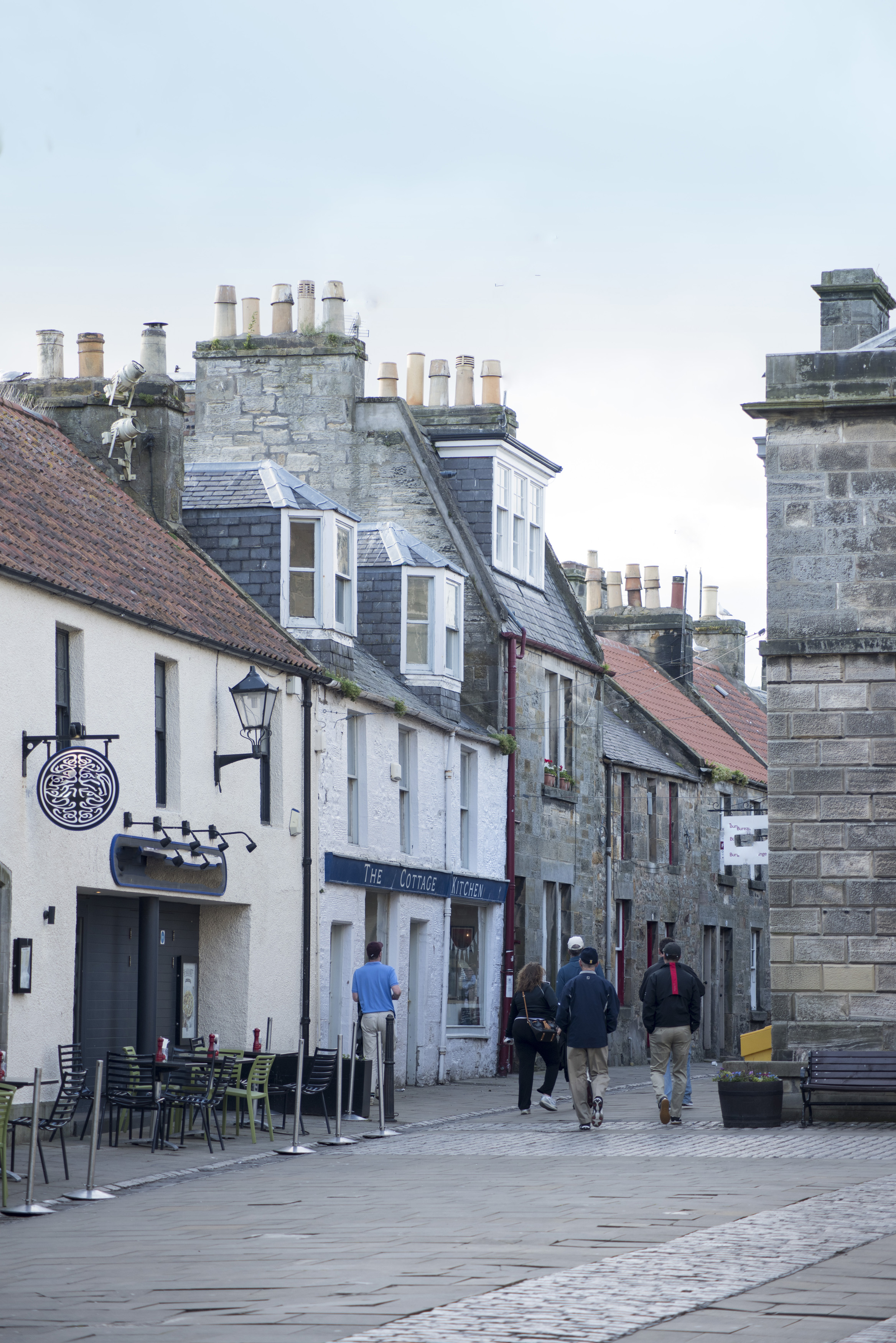 an image of Rear view of various tourists walking down street in front of small cafe at Saint Andrews, Scotland