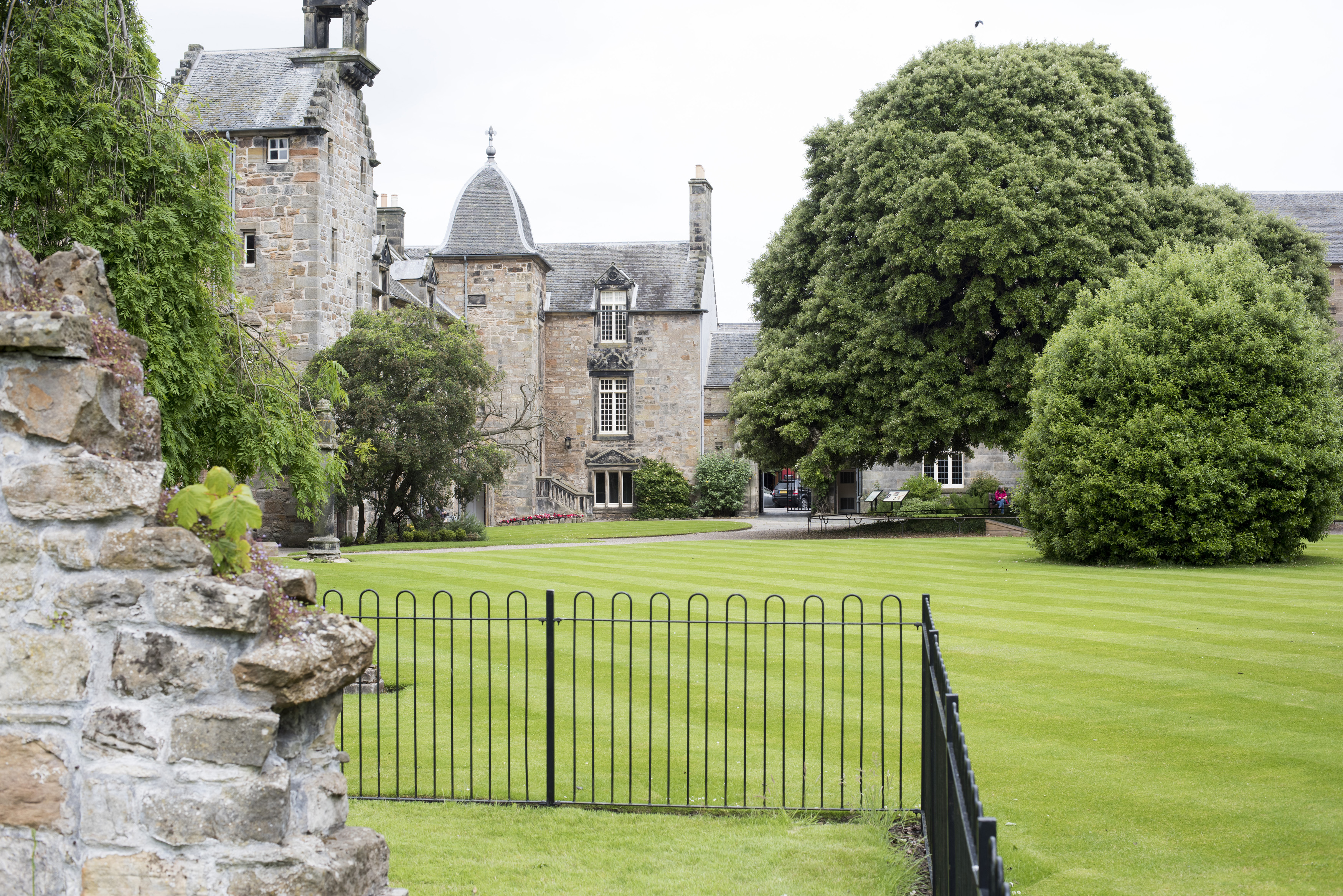 an image of Gated university grounds with lush green lawn and adjoining stone buildings