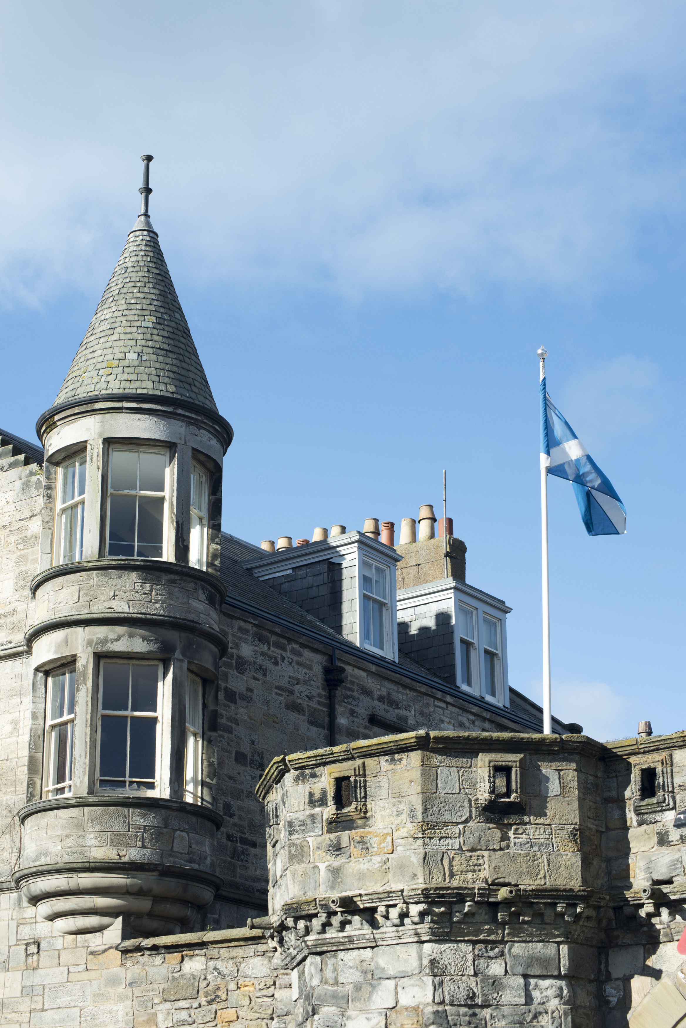 an image of Lovely stone building at the west port, st andrews, with conical roofed tower and rookery with lone flag flying on white pole