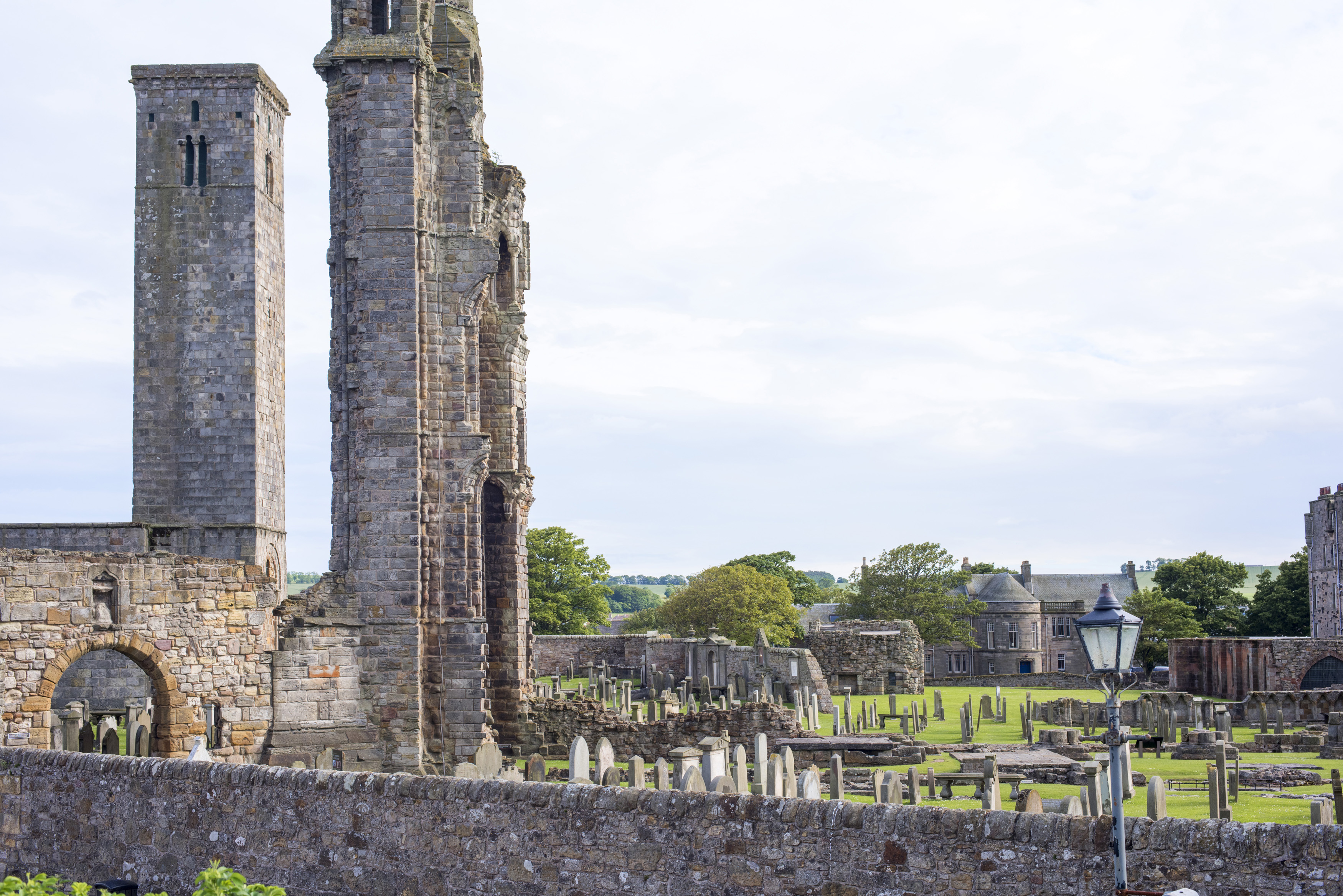 an image of Stone barrier in front of old graveyard and towers of Saint Andrews Cathedral in Scotland with copy space in sky