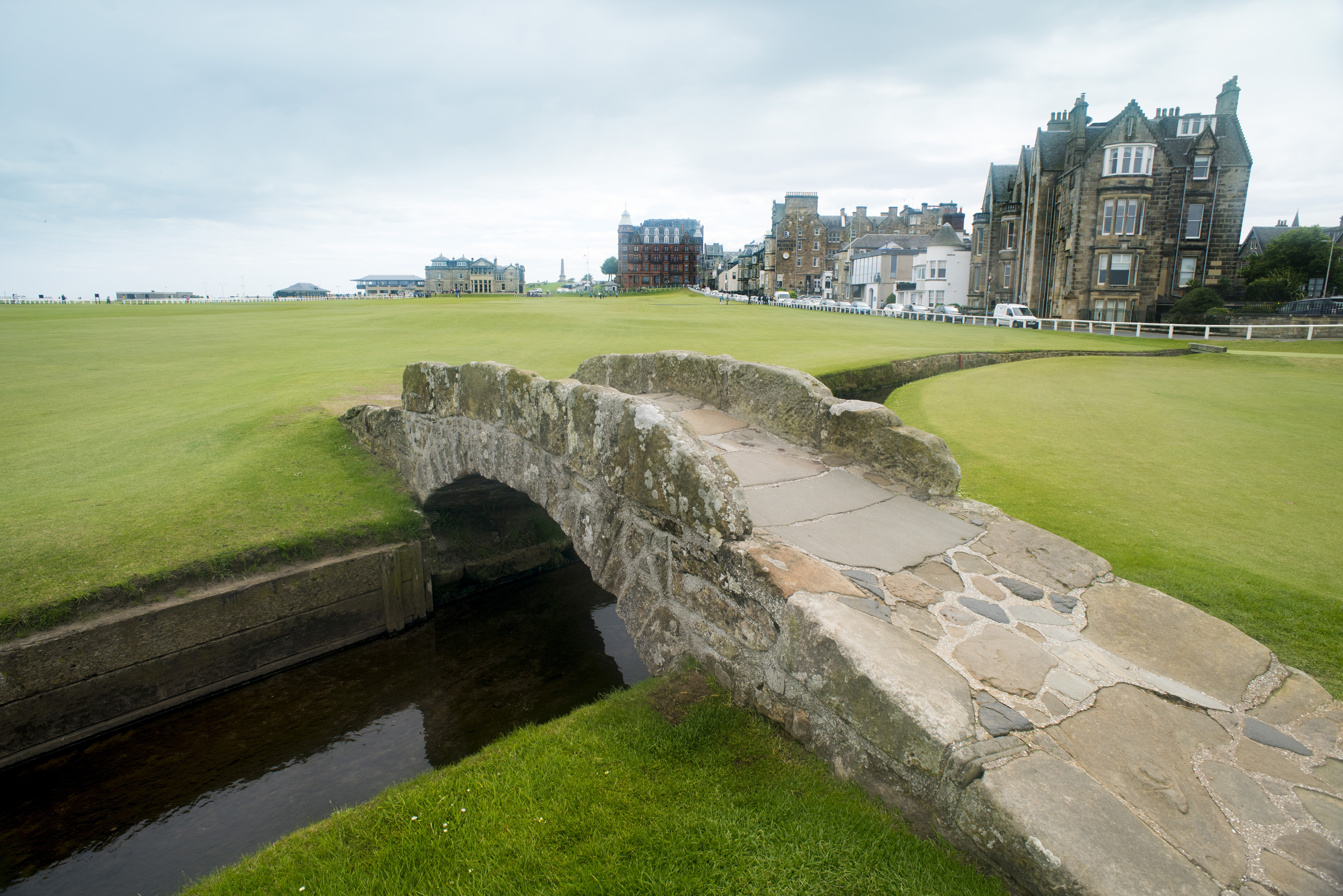 an image of Green grass covered golf course with little stone Swilken bridge in Saint Andrews, Scotland