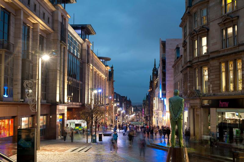 Buchanan Street in Glasgow at night lined with colourful shops and pedestrian shoppers walking the sidewalks