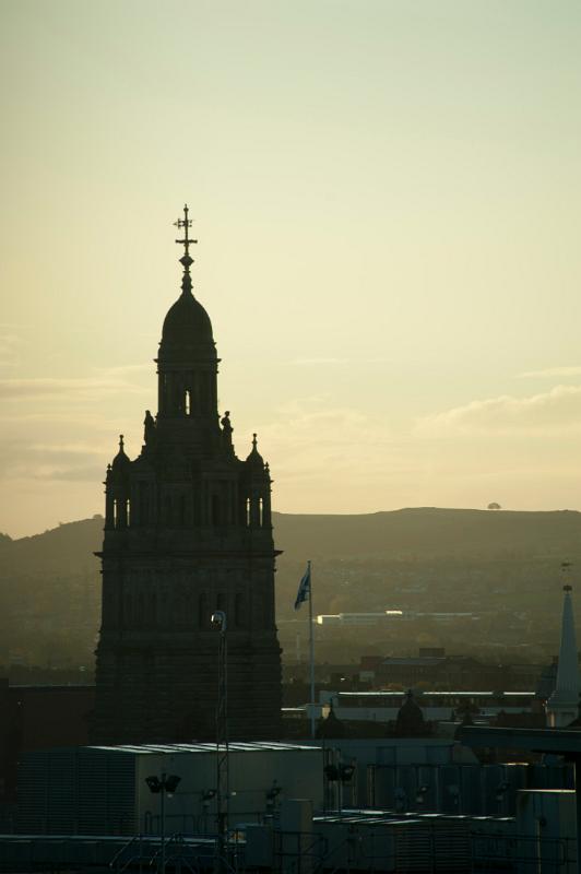 Glasgow City Hall silhouette at dusk towering over the rooftops of the city against a glowing horizon