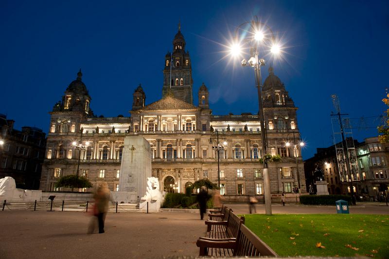 George Square, Glasgow at night looking towards the historical external facade of the Glasgow City Council building with pedestrians crossing the square