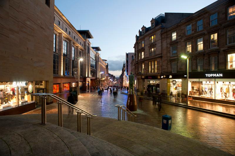 Buchanan Street in central Glasgow at night with the windows of the shops illuminated with bright lights reflected on the street below