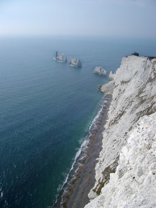 View along the coastline of the Isle of Wight showing the steep cliffs, beach and the Needles, a row of eroded chalk stacks rising from the ocean