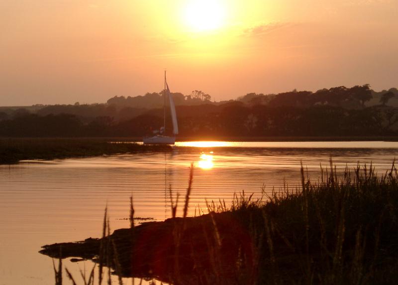 River Yar, Isle of Wight, which starts at Freshwater Bay, on the south coast of the island and flows only a few miles north to Yarmouth viewed at sunset with the orange sun reflected in the calm water