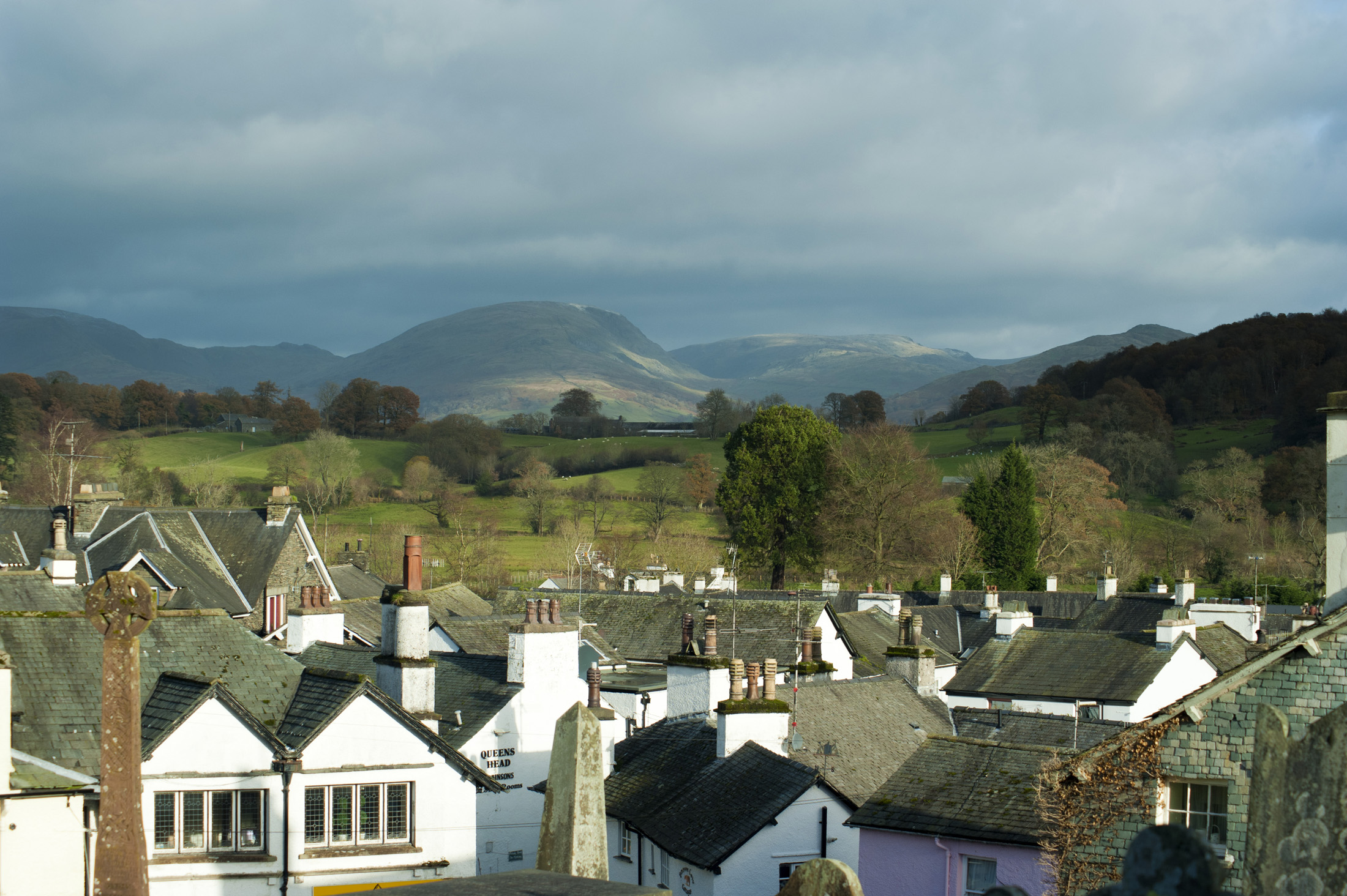 an image of View over the rooftops of Hawkshead village towards lush green countryside and Wansfell Pike in the Lake District