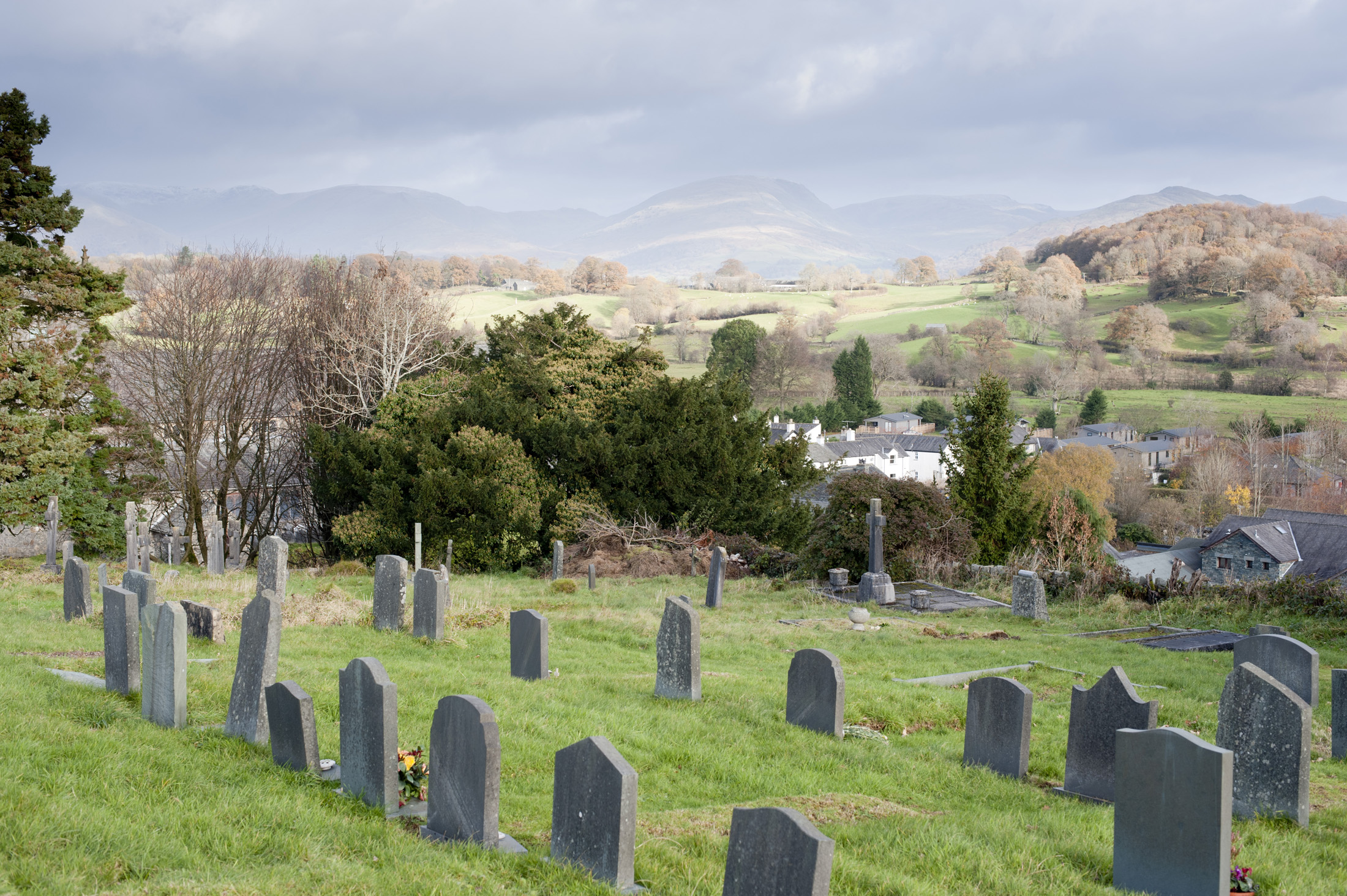 an image of Gravestones in the churchyard at Hawkshead in the English Lake District with a view to beautiful lush green countryside and hills beyond