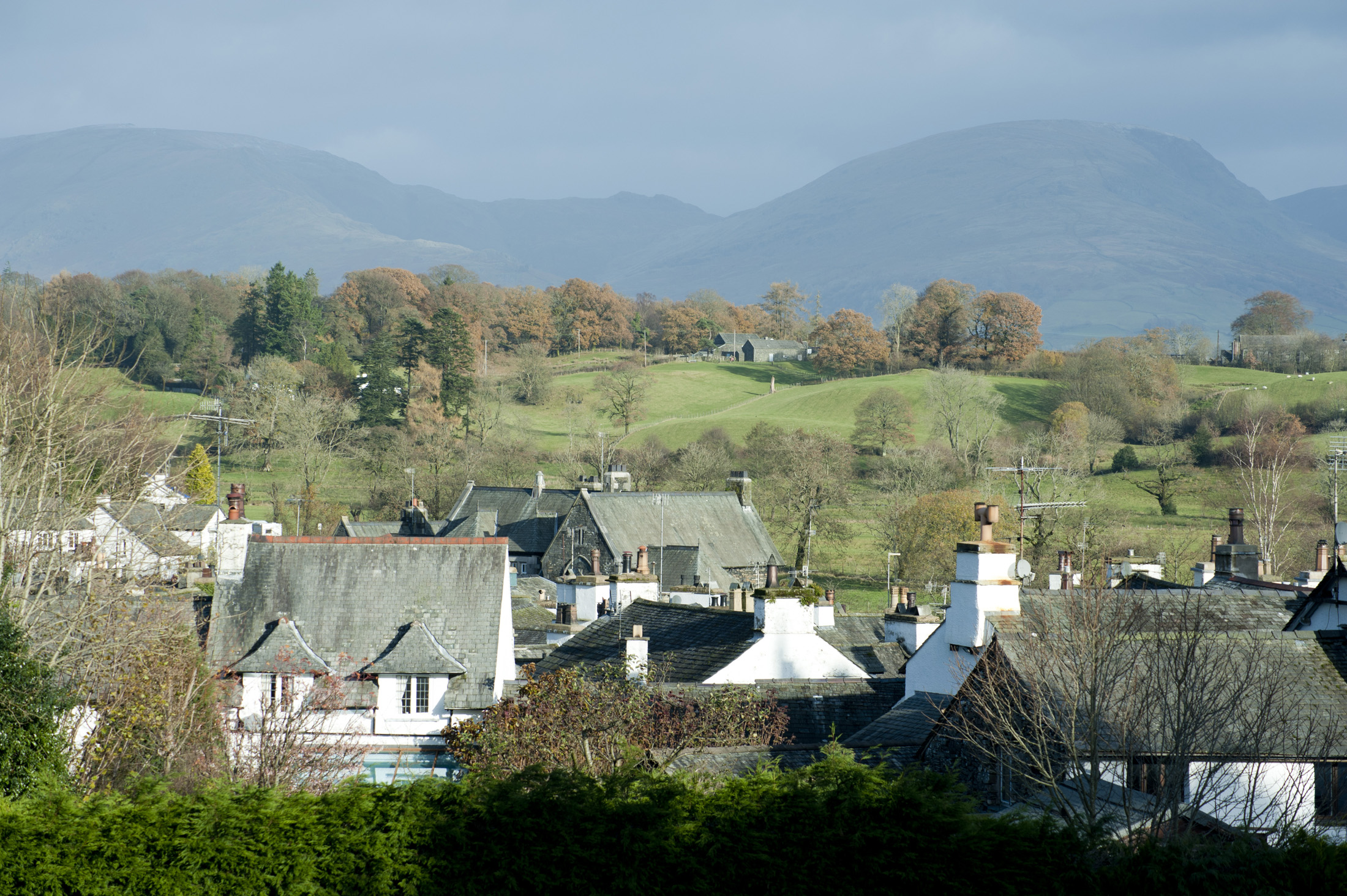 an image of View over the rooftops of the whitewashed cottages of Hawkshead village to Red Screes in the English Lake District in Cumbria